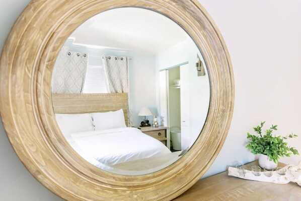 A bedroom with a large mirror, a bed, a nightstand, and a potted plant.
