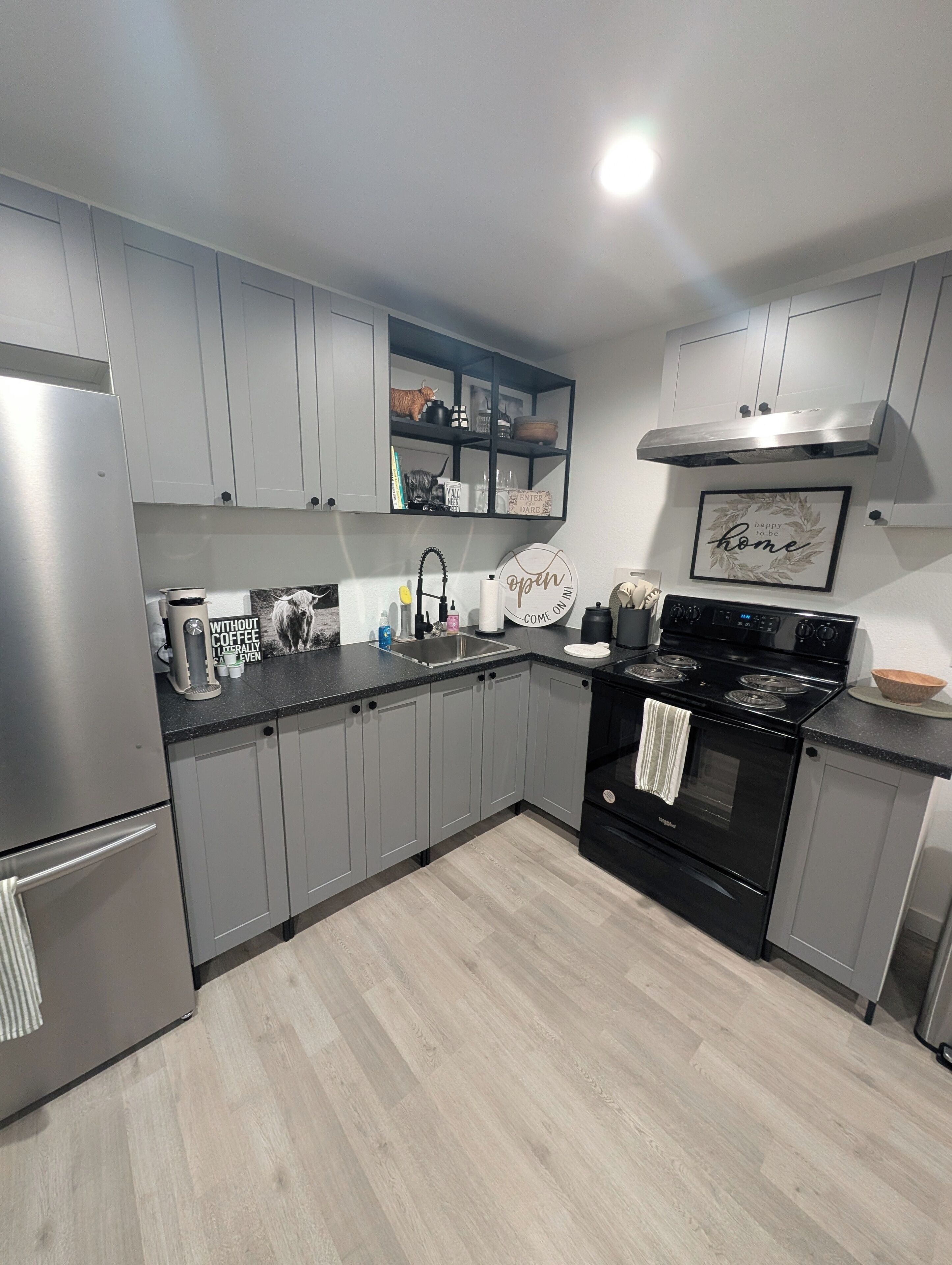 A modern kitchen with grey cabinets, stainless steel appliances, and a black stove.