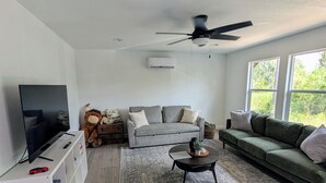 A modern living room with a grey sofa, a coffee table, a TV on a white stand, and a ceiling fan. - Wonderful Pondview Cottage in College Station (College Station)