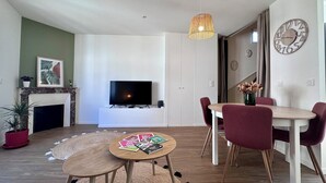 Una sala de estar moderna con televisor de pantalla plana, chimenea, comedor con mesa y sillas, y un reloj decorativo en la pared.
