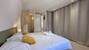 Una habitación de hotel con una cama grande, suelo de madera, una mesita de noche con lámpara y un baño visible a través de una puerta abierta.