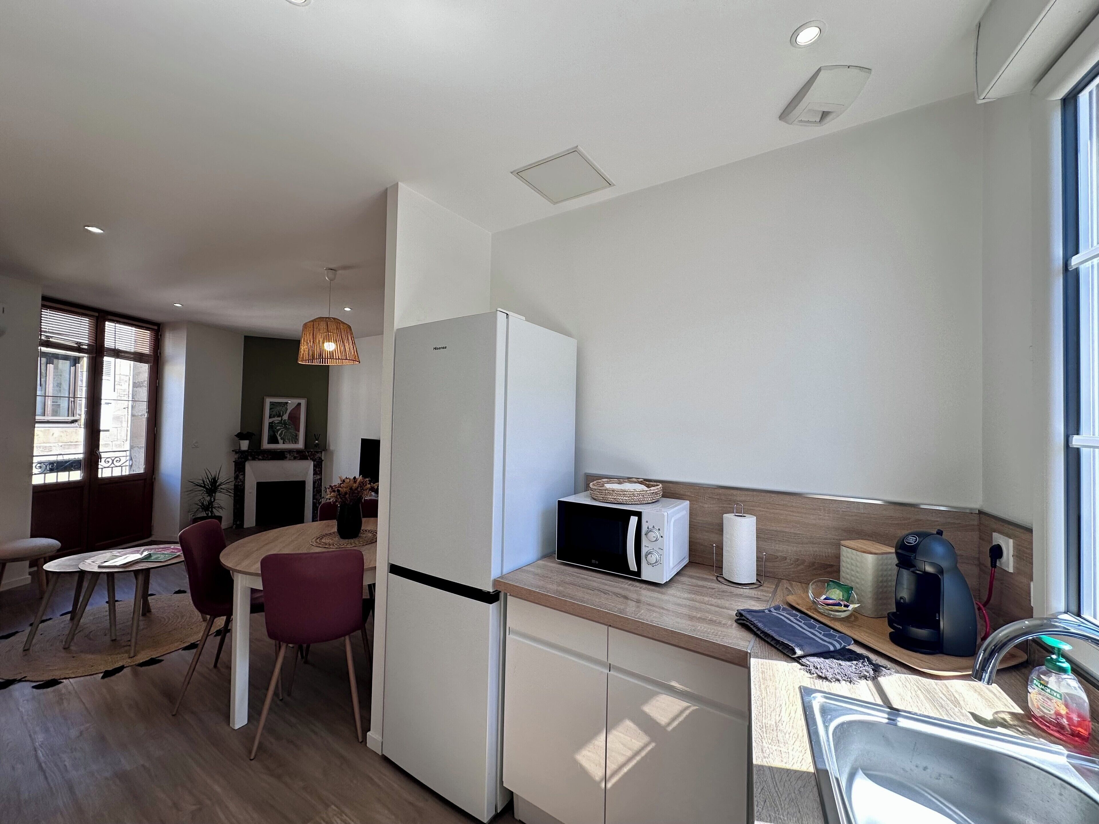 A modern kitchen with a refrigerator, microwave, and coffee maker. There is a dining area with a table and chairs.