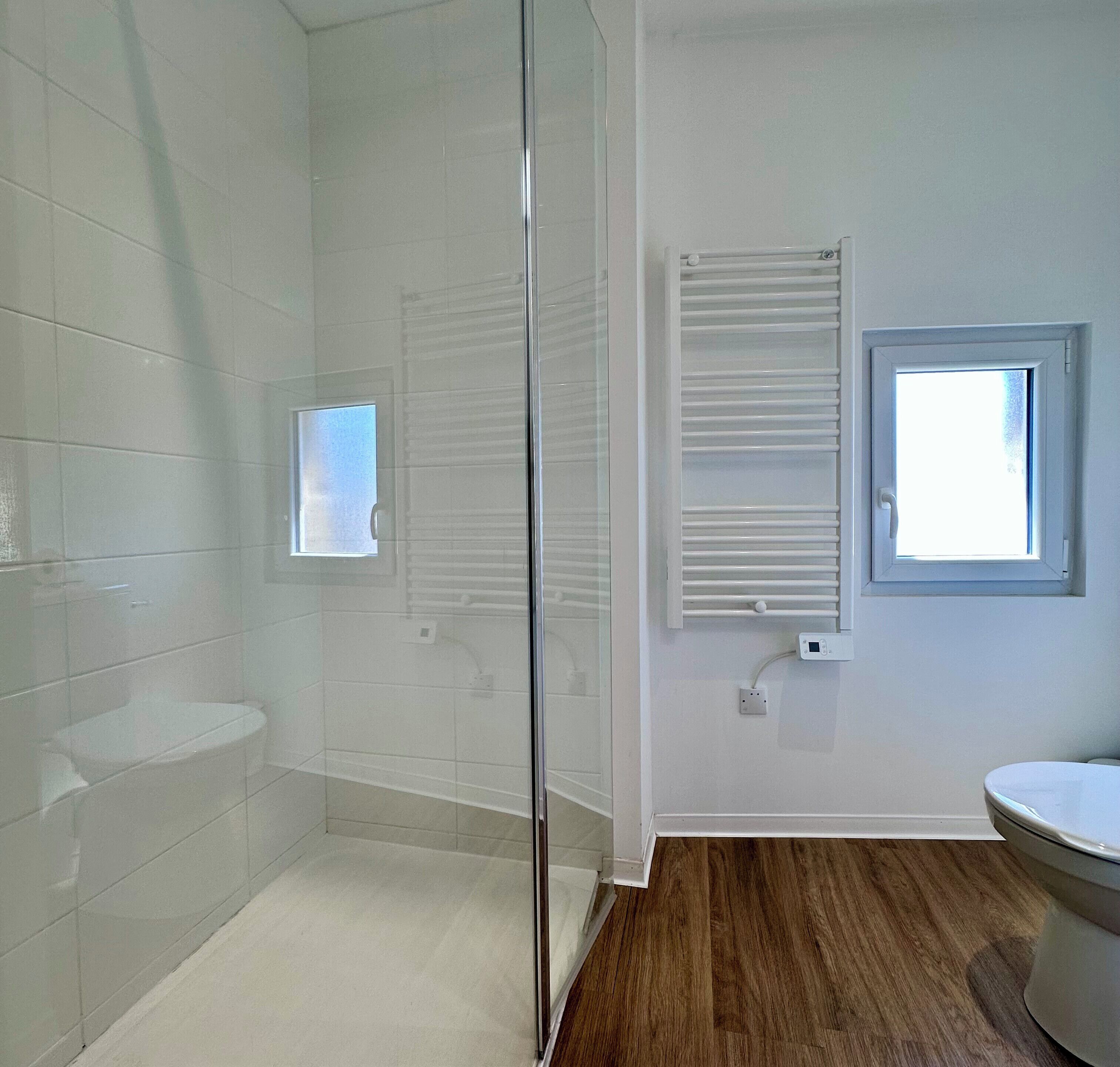 A bathroom with a glass shower enclosure, a toilet, a sink, a window, and a towel rack.