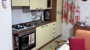 A compact kitchen with a gas stove, oven, and wooden cabinets. There is a small dining area with a table and a chair. - VACATION HOME OF THE FISHERMAN (Tonnarella)