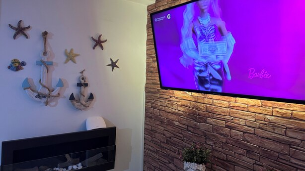A room with a flat-screen TV mounted on a brick wall, decorative anchors and starfish on the wall, and a small plant on the floor. - VACATION HOME OF THE FISHERMAN (Tonnarella)