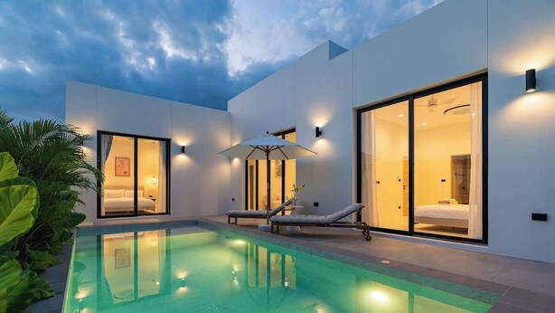 A modern hotel with a swimming pool, large glass doors, and outdoor seating.