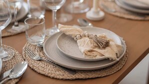 A dining table set with plates, cutlery, and glasses, with a candle and a rolled napkin on the table.