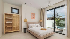 A bedroom with a bed, a wooden wardrobe, a ceiling fan, and a view of a swimming pool.