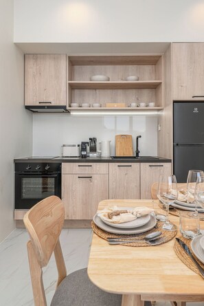 Une cuisine moderne avec des meubles en bois, un four encastré, un réfrigérateur noir et une table à manger pour deux personnes.