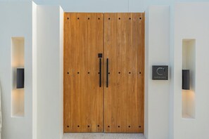 Een grote houten deur met een zwarte handgreep en twee verticale staven, omlijst door wandlampen en een bord met het nummer '7'.