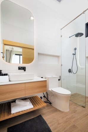 Une salle de bain moderne avec un meuble-lavabo en bois, un grand miroir, des toilettes et une douche séparée par une paroi de verre.