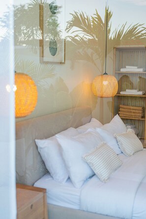 Un lit avec une literie blanche et des oreillers à rayures, une suspension en fibres tressées et une étagère avec des serviettes pliées.