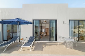 Un patio extérieur moderne, doté de chaises longues, d’une table et d’un parasol.
