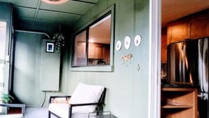 A room with a large window, a chair, a small table, and a kitchen area visible through the window. - Downtown Designer Duplex close to Beach! Spa Tub, Sunroom, Game Room, EV & more! (Long Beach)