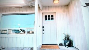 A white building with a front door, a window, and a small porch area. - Downtown Designer Duplex close to Beach! Spa Tub, Sunroom, Game Room, EV & more! (Long Beach)