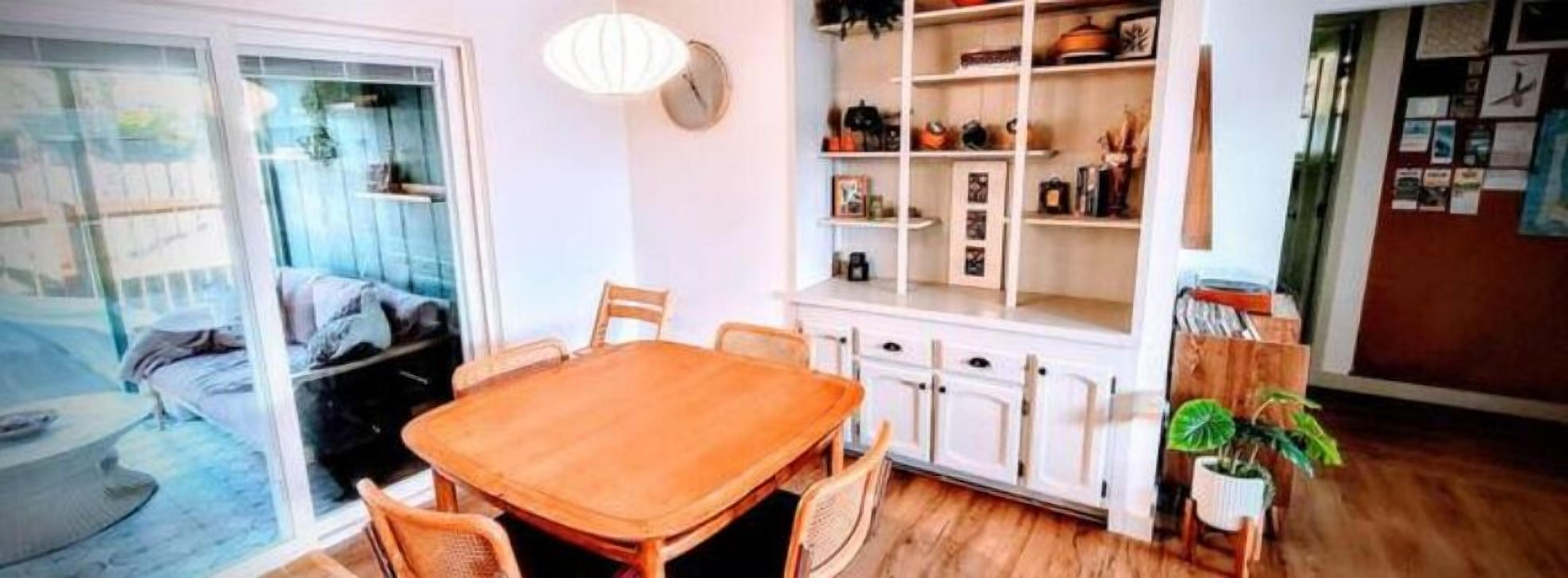 Ein Essbereich mit einem Holztisch und Stühlen, einer weißen Schrank mit Regalen und einer Topfpflanze.