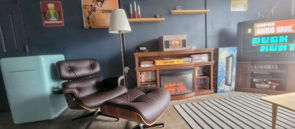 Ein Wohnzimmer mit Ledersessel, Kamin, Fernseher, der 'SUPER MARIO BROS. DUCK HUNT' zeigt, und Bücherregal.