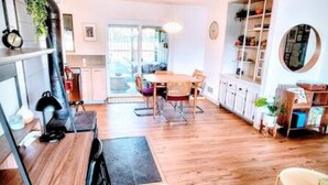 A cozy kitchen with wooden flooring, a dining table, and chairs. There is a bookshelf with various items and a round mirror on the wall. - Downtown Designer Duplex close to Beach! Spa Tub, Sunroom, Game Room, EV & more! (Long Beach)