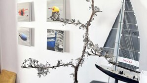 A room with a wall-mounted sailboat model, a black ottoman, and various framed artworks.