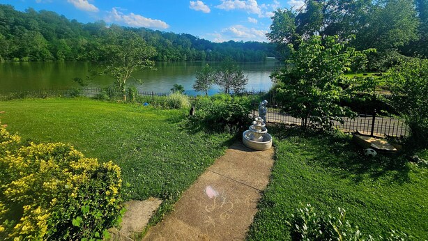 A serene lakeside view with a pathway leading to a gazebo, surrounded by lush greenery and trees. - Charming 1850s Victorian on the Monongahela River (Greensboro)