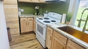 A kitchen with wooden cabinets, a white stove, a microwave, and a window with a view of greenery. - Charming 1850s Victorian on the Monongahela River (Greensboro)