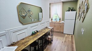 A kitchen with a wooden table, bar stools, a refrigerator, and a window with curtains. - Charming 1850s Victorian on the Monongahela River (Greensboro)