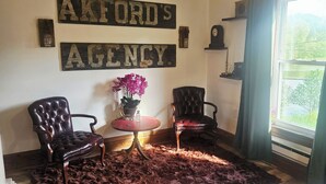 A room with two leather chairs, a small table with a vase of flowers, and a rug on the floor. There are two signs on the wall reading "Auckland's Agency". - Charming 1850s Victorian on the Monongahela River (Greensboro)