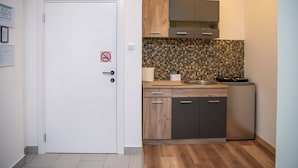 A compact kitchen with a white door, a no-smoking sign, wooden cabinets, a tiled backsplash, and a built-in oven. - Elegant apartment with Balcony & Free Parking (Subotica)