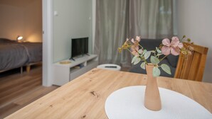 A wooden table with a white placemat and a vase with flowers. A bed and a television are visible in the background. - Elegant apartment with Balcony & Free Parking (Subotica)