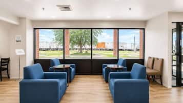 Une pièce dotée d’une grande fenêtre, d’un coin salon avec des canapés et des tables, et offrant une vue sur un bâtiment et des arbres à l’extérieur.