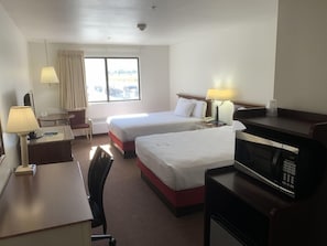 A hotel room with two beds, a desk with a lamp, a chair, a microwave, and a window with curtains. - Days Inn by Wyndham Lake Point (Tooele)