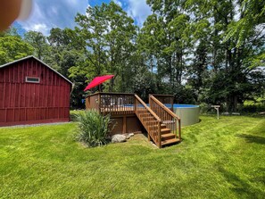 A wooden deck with a red umbrella, a swimming pool, and a red barn.