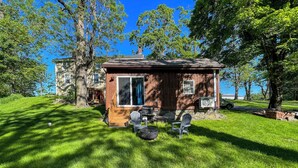 A small wooden cabin with a deck, outdoor seating, and a view of a lake.