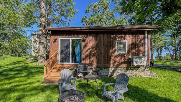 A wooden cabin with a covered deck, outdoor seating, and a fire pit.