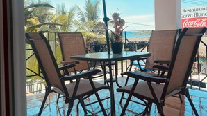 An outdoor patio with a table and chairs, a large umbrella, and a view of the beach and palm trees. - Bungalows Garza Blanca a Pie de Playa (San Blas)