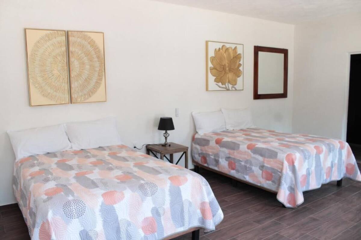 A room with two beds, each with a patterned bedspread, a small table with a lamp, and wall art.