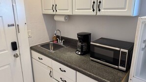 A compact kitchen with white cabinets, a stainless steel sink, a coffee maker, and a microwave. - Charming studio in sunny Miami Beach with ocean view! (Miami Beach)