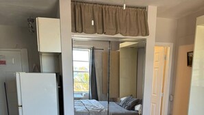 A compact bedroom with a bed, a wardrobe, a ceiling fan, and a refrigerator. - Charming studio in sunny Miami Beach with ocean view! (Miami Beach)