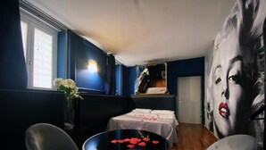 A room with a bed, a table with rose petals, and a large poster.