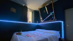 A bedroom with a bed, a mirror, and LED strip lighting along the ceiling edge.
