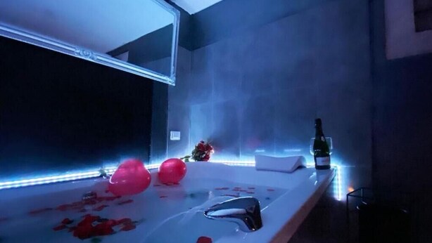 A modern bathroom with a large mirror, a white sink, and a bottle of alcohol on the counter.