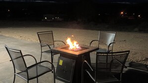 An outdoor seating area with a fire pit table and four chairs.
