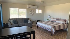 A spacious room with a large bed, a sofa, a dining table, and a clock on the wall.