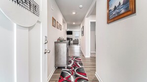 A hallway with a checkered wall decoration, a framed picture, and a patterned carpet. - The Magnolia Retreat (Omaha)