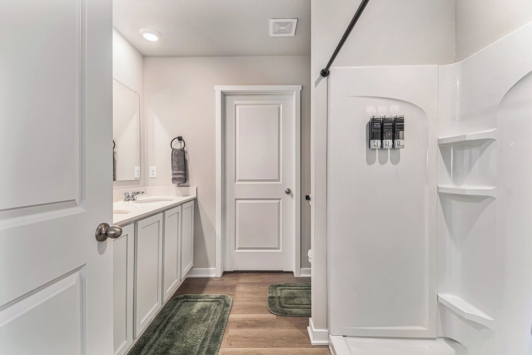 A hallway with a white door, a bathroom with a sink and mirror, and a green rug on the floor.