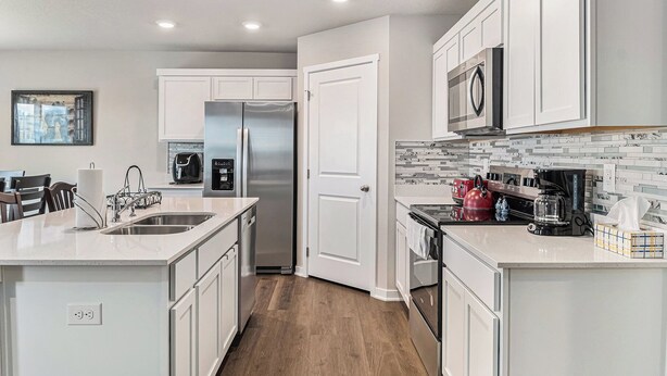 A modern kitchen with white cabinetry, stainless steel appliances, and a tiled backsplash. - The Magnolia Retreat (Omaha)