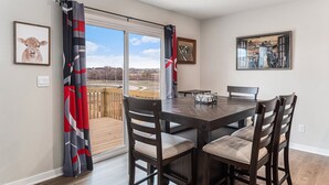 A dining area with a wooden table and chairs, a view through a glass door, and two framed pictures on the walls. - The Magnolia Retreat (Omaha)
