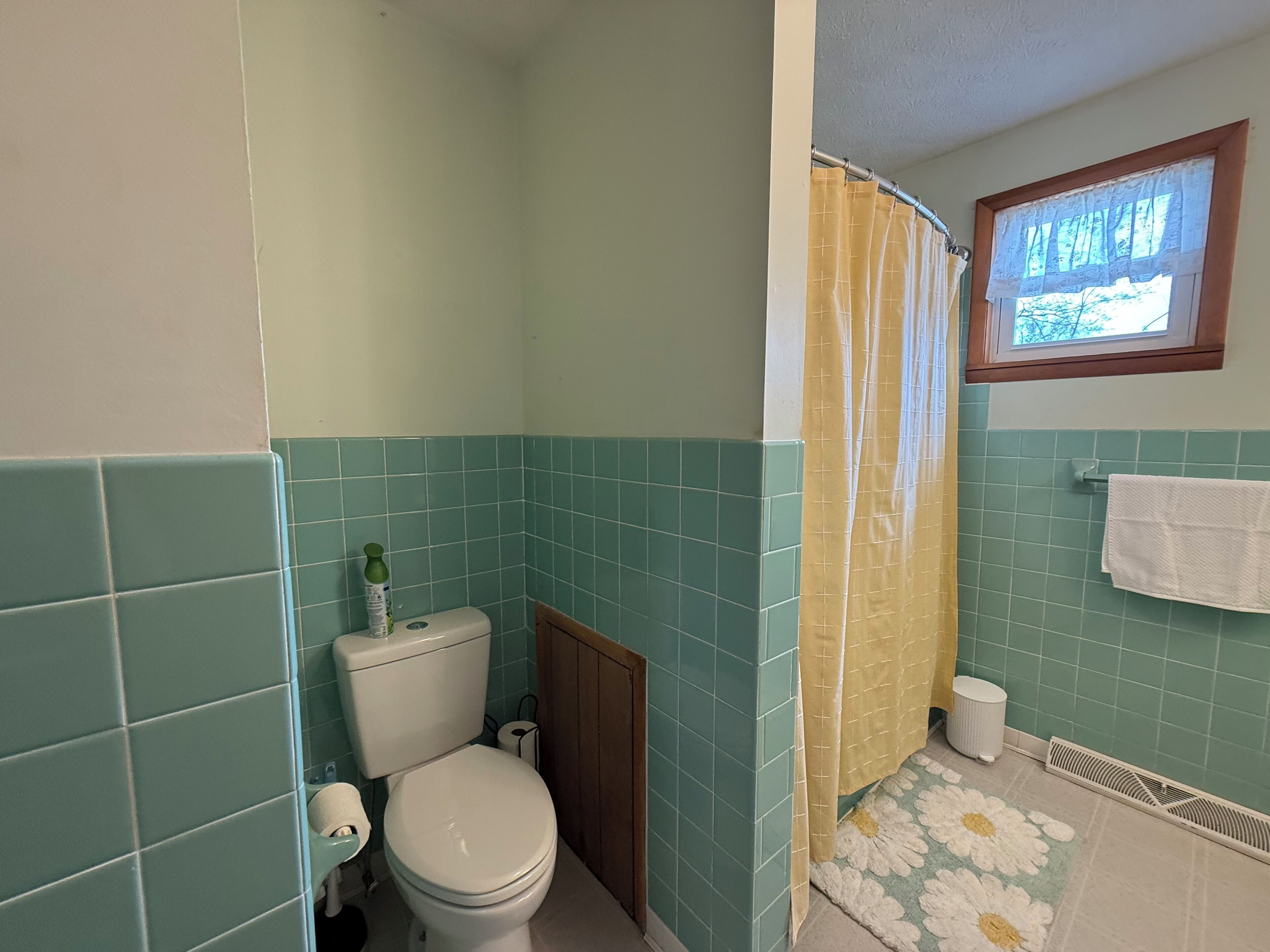 Een badkamer met een toilet, douchegordijn en een raam.