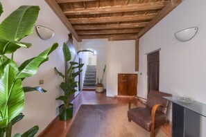 A hallway with a wooden ceiling, a potted plant, a brown leather chair, and a glass table.
