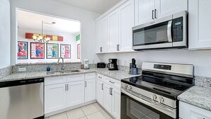 Una cocina moderna con gabinetes blancos, microondas integrado, estufa y lavavajillas.